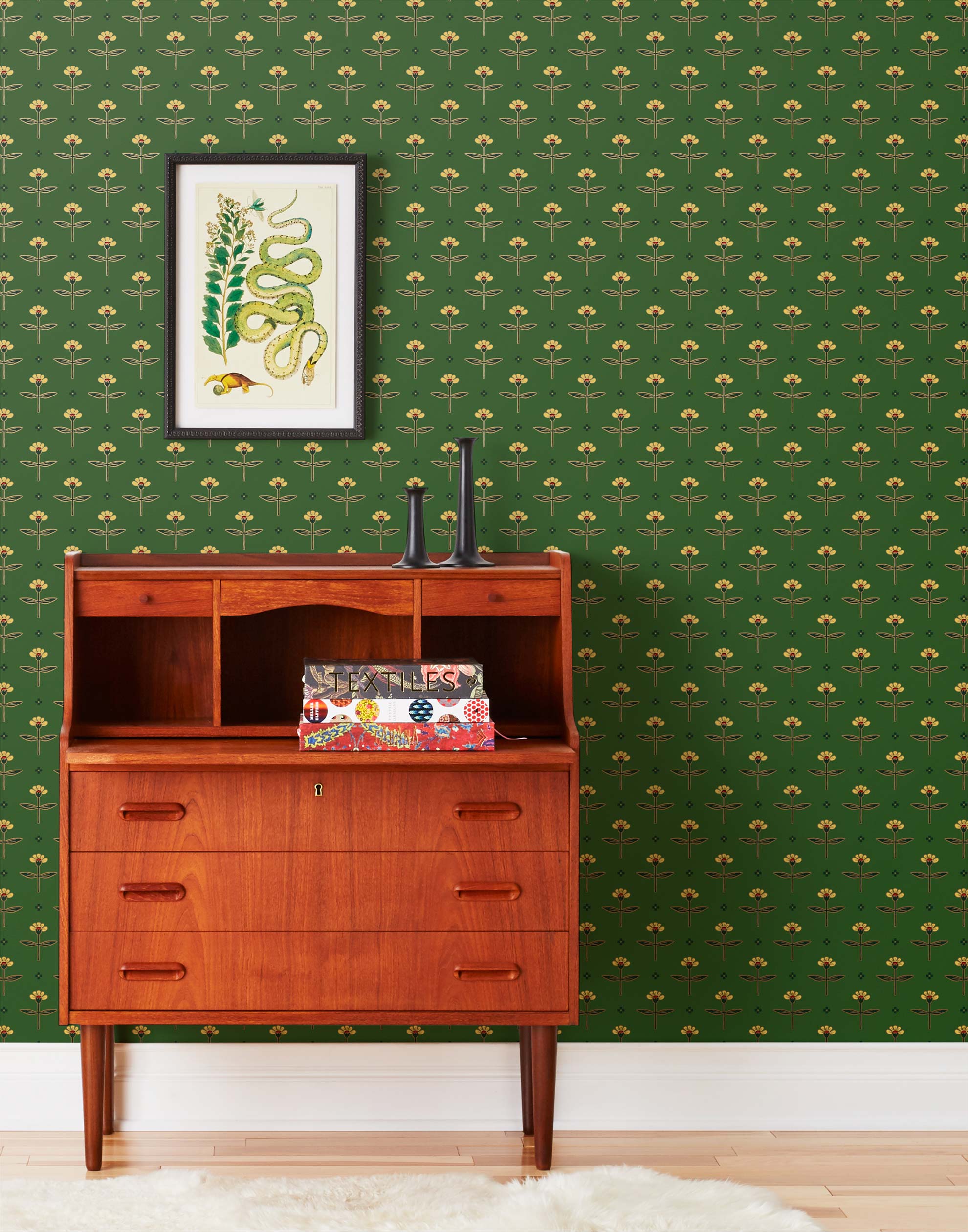 Zinnia (Juniper) Wallpaper mixes a geometric layout with the soft details of the zinnia flower. Yellow, gold, and red illustration on a green ground.