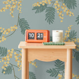 Wallpaper with yellow acacia flowers and green leaves on a dusty blue background | Schoolhouse + Hygge & West